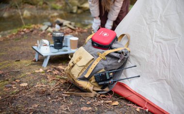 Kamp çadırının yanındaki sırt çantasındaki kırmızı ilk yardım çantası. Ormanda yaralanmalar ve hasar. Yürüyüşe çıkmış tıbbi destek kavramı. Yolculukta yaralanma ihtimaline karşı acil yardım.