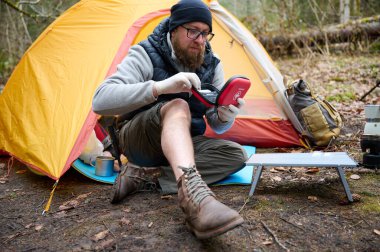 Ormandaki çadırın yakınındaki ilk yardım çantasını kullanan yaralı bacaklı bir yürüyüşçü. Stresli bir yürüyüşçü dağda kırık diziyle tek başına şikayet ediyor..