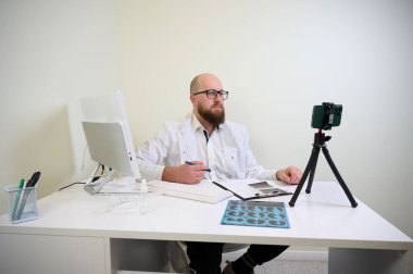 Beyaz önlüklü doktor modern klinikteki webcam üzerinden online danışmanlık yapıyor. Teletıp kavramı, uzaktan sağlık, sanal randevu, dijital sağlık.