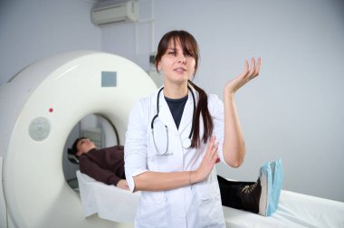 Genç bayan radyolog tomografi odasında kalıyor. Klinikte çalışıyorum. Güzel doktor kameraya, tomografiye ve MRI 'ya bakıyor. Üniformalı doktor.