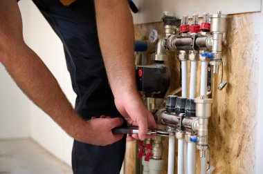 Adam yeni bir dairede ısıtma sistemini ayarlıyor. Tesisatçı merkezi sistem vanalarındaki ısıyı ayarlıyor. Servis elemanı ısıtma sistemini ayarlıyor. Yeraltı ısıtma sistemi. Ekin görünümü
