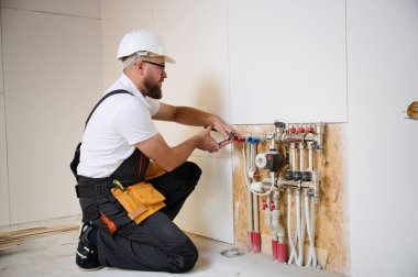 Adam yeni bir dairede ısıtma sistemini ayarlıyor. Tesisatçı merkezi sistem vanalarındaki ısıyı ayarlıyor. Servis elemanı ısıtma sistemini ayarlıyor. Yeraltı ısıtma sistemi. Adam boruyu kontrol ediyor