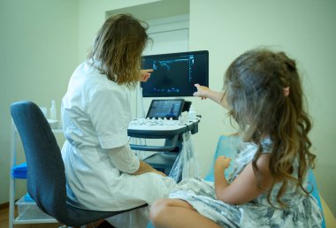 Klinikte küçük bir çocuğa danışmanlık yapan çocuk doktoru. Çocuk doktoru, ultrason tarayıcısının yanındaki küçük çocuğu muayene ediyor. Tıp bürosu. Ultrason taraması için hazırlanılıyor.
