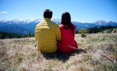 İki yürüyüşçü bir dağ sırtında mola veriyor. Sırt çantalı sportif çift, karlı dağların arka planında duruyorlar..