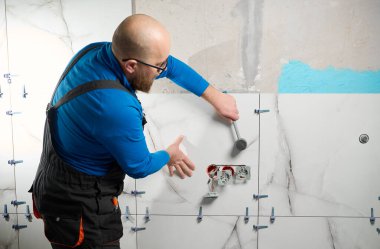 Yeni dairenin duvarına seramik granit döşeme döşeyen adam. Tesisatçı müşteri banyosuna seramik fayanslar yerleştiriyor, evi satmaya hazırlanıyor. Döşeme seviyelendirme sistemi.