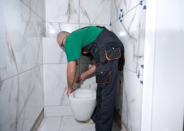 Tesisatçı tuvalet kuruyor. Modern tuvalet tesisatı. İşçi duvara duvara duvara asılmış tuvalet kuruyor. Tuvalet tesisatı. Profesyonel tesisatçı tuvaleti tamir ediyor..