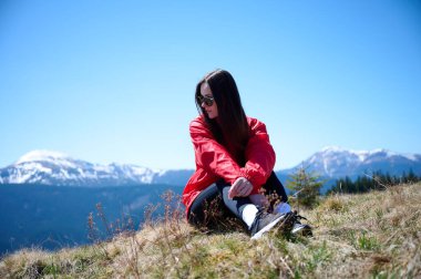 Yüksek dağların tepesinde oturan kadın yaz manzarasının tadını çıkarıyor. Uçurumun kenarında oturan ve güneş vadisine ve dağlara bakan bir kız. Mutlu gezgin güneşli günün tadını çıkarıyor