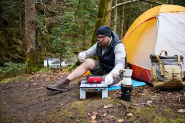 Ormandaki çadırın yakınındaki ilk yardım çantasını kullanan yaralı bacaklı bir yürüyüşçü. Stresli bir yürüyüşçü dağda kırık diziyle tek başına şikayet ediyor..