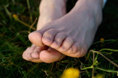 Yeşil çimlerin üzerinde kadın bacakları. Çimlerin üzerindeki ayaklara yakından bak. Dişinin çıplak ayakları çimlerin üzerinde. Güneşte dinlenen kız. Rahatlama konsepti ve doğayla bağlantı.