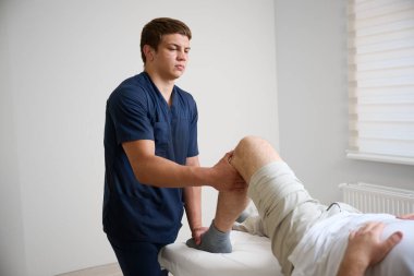 Modern tıp kliniğindeki rehabilitasyon seansında hastanın diz eklemlerini muayene eden fizyoterapist. Yaraları için ortopedik tedavi ve fizik tedavi gören bir adam..