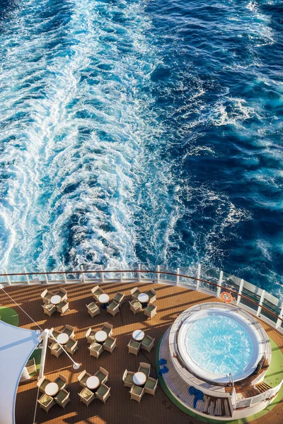 Deck of a sailing cruise ship with a jacuzzi and some empty tables and chairs.