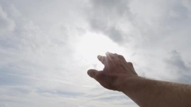 Mans hand palm reaching toward the sunshine into a cloudy sky