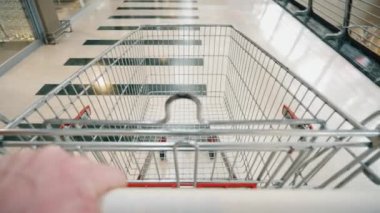 Empty shopping cart. A person hand pushing a shopping cart in a supermarket corridor