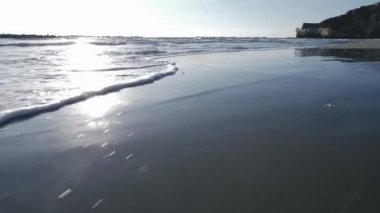 Dalgalar kumlu deniz kıyısında ilerliyor. Kamera sahil boyunca el kamerasıyla çekilmiş. Yüksek kaliteli görüntüler 4K