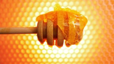 Taze bal, ahşap bir bal kaşığının üzerinden akıyor. Arka planda bal petekleri.