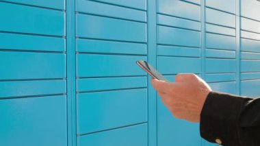 Automated parcel locker. Person receives a parcel from a courier service by opening a mailbox through an application on his phone