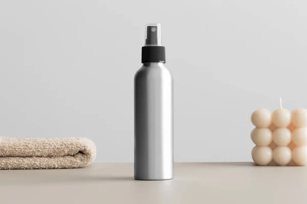 Aluminium cosmetic spray bottle mockup with a candle and a towel on the beige table.