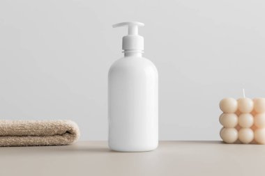 White cosmetic liquid soap dispenser bottle mockup with a candle and a towel on the beige table.