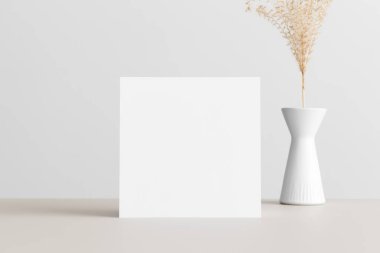 Square invitation card mockup with a dried flower decoration  on the beige table. 5x7 ratio, similar to A6, A5.