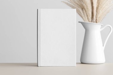Bej masa üzerinde sazlık pampa süslemesi olan beyaz kitap modeli..