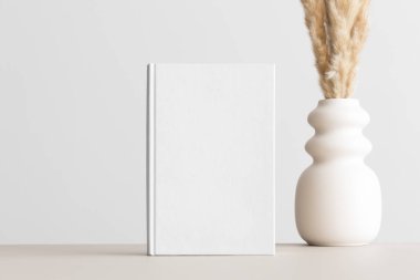 Bej masa üzerinde pampa süslemesi olan beyaz kitap modeli..
