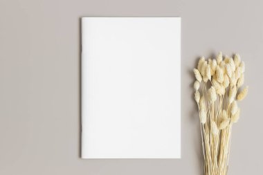 Bej masasının üzerinde bir buket kuru çiçek olan dergi modeli..