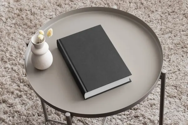 Black book mockup with a dried flower decoration on the beige table.