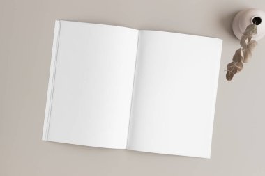 Bej masasında okaliptüs olan açık dergi modeli.