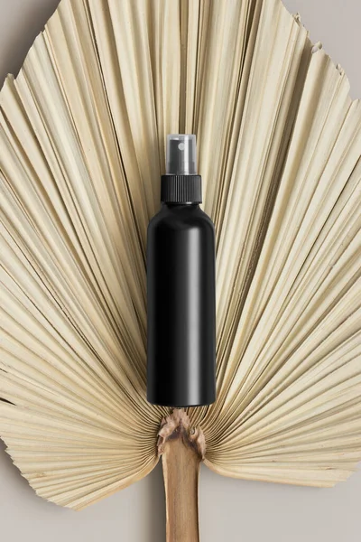 Black cosmetic spray bottle mockup with a palm leaf on the beige table.