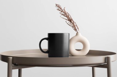 Siyah kupa modeli ve bej masa üzerinde kuru bir çiçek süslemesi..