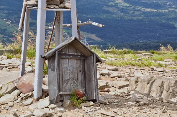 Wooden structure in the shape of a cottage, memory, tombstone with a candle, supported by a metal steel structure in the mountains, rocky ground, mountains in the background, Bieszczady National Park