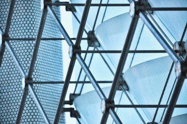 Cam paneller ve metal kirişlerden oluşan karmaşık bir geometrik yapı, karmaşık mimari tasarımı ve ışık ve gölgelerin etkileşimini vurguluyor.