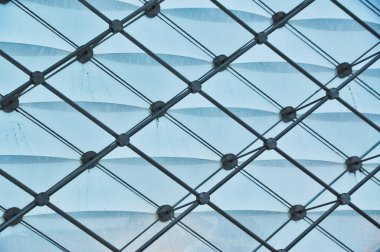 Cam paneller ve metal kirişlerden oluşan karmaşık bir geometrik yapı, karmaşık mimari tasarımı ve ışık ve gölgelerin etkileşimini vurguluyor.