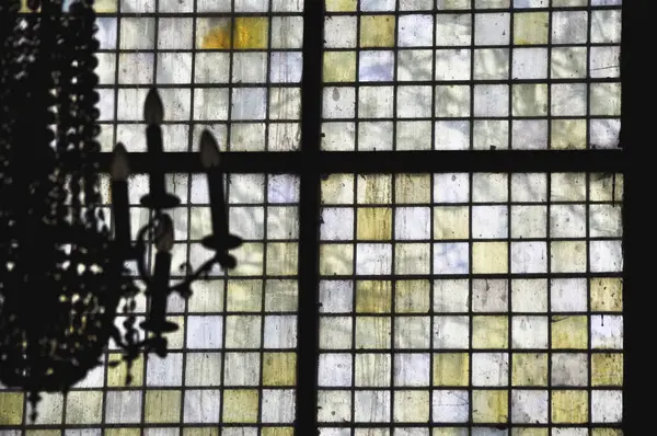 stock image Ornate chandelier silhouetted against a colorful opaque milky glass mosaic window in a black frame