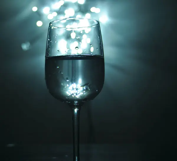 Suyla dolu bir bardak, mavi tonlar, arka plandaki ışıklardan gelen beyaz bokeh, küçük ışık kaynakları.
