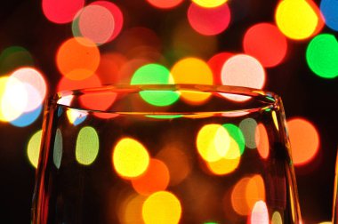 Suyla dolu şeffaf şarap kadehleri, arka plandaki ağaçta renkli Noel ışıkları.
