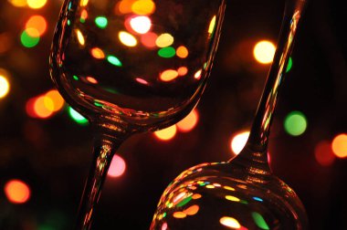 Suyla dolu şeffaf şarap kadehleri, arka plandaki ağaçta renkli Noel ışıkları.