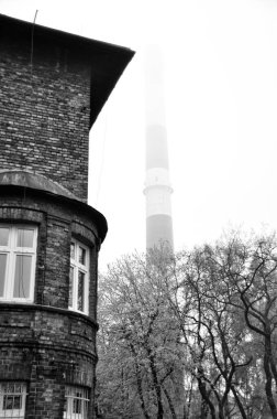 Two tall white and red chimneys of a power plant visible above trees and brick buildings clipart