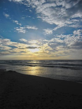 Güneş batarken Baltık Denizi kıyısında hafif bulutlu ve hafif dalgalı bir Polonya plajı.