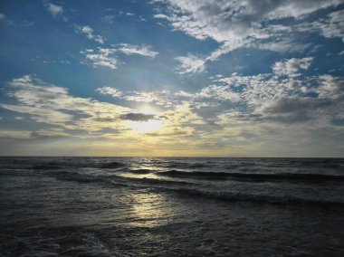 Güneş batarken Baltık Denizi kıyısında hafif bulutlu ve hafif dalgalı bir Polonya plajı.