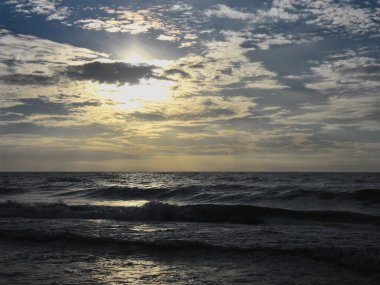 Güneş batarken Baltık Denizi kıyısında hafif bulutlu ve hafif dalgalı bir Polonya plajı.