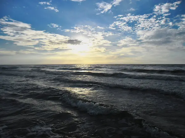 Güneş batarken Baltık Denizi kıyısında hafif bulutlu ve hafif dalgalı bir Polonya plajı.