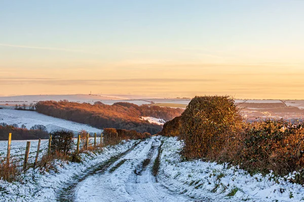 A country road near Ditchling Beacon in Sussex, with snow on the ground and a sunset sky overhead