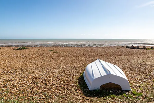 Sahildeki çakıl taşı sahili üzerinde Sussex 'teki Pett Level' de ön planda ters dönmüş bir tekne var.