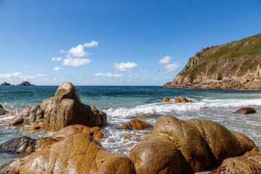 Cornwall kıyısındaki Porth Nanven plajında kaya oluşumları, mavi bir gökyüzü ile
