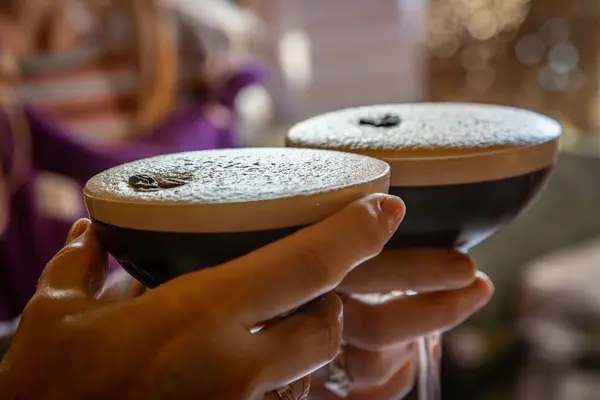 A close up of hands holding espresso martini cocktails, with a shallow depth of field