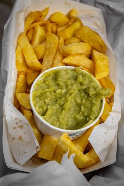 A tub of mushy peas and freshly cooked chips from a chip shop, with selective focus clipart