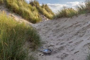 A discarded disposable bbq in sand dunes, on a summer's day clipart