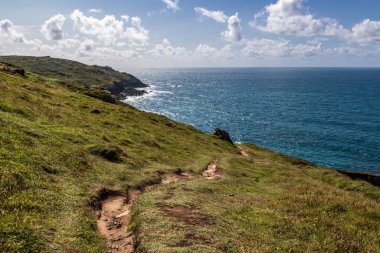 Engebeli Cornish kıyı şeridinde mavi gökyüzü boyunca uzanan patikaya bakıyorum.