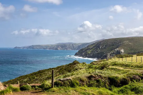 Pendeen Deniz fenerinin yakınındaki Cornish sahil şeridine bakıyorum, tepemizde mavi bir gökyüzü var.